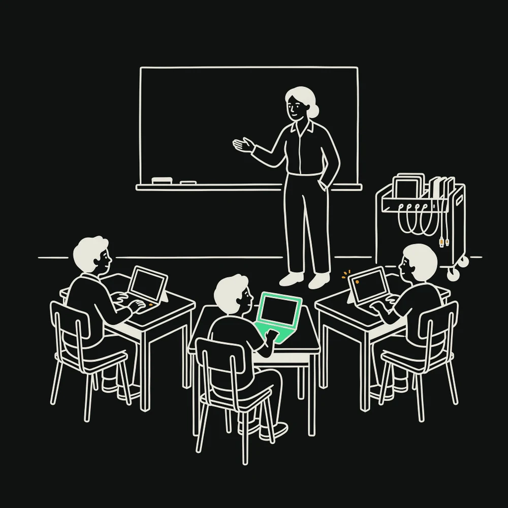 A teacher beside a whiteboard turning towards students working at desks with laptops open.